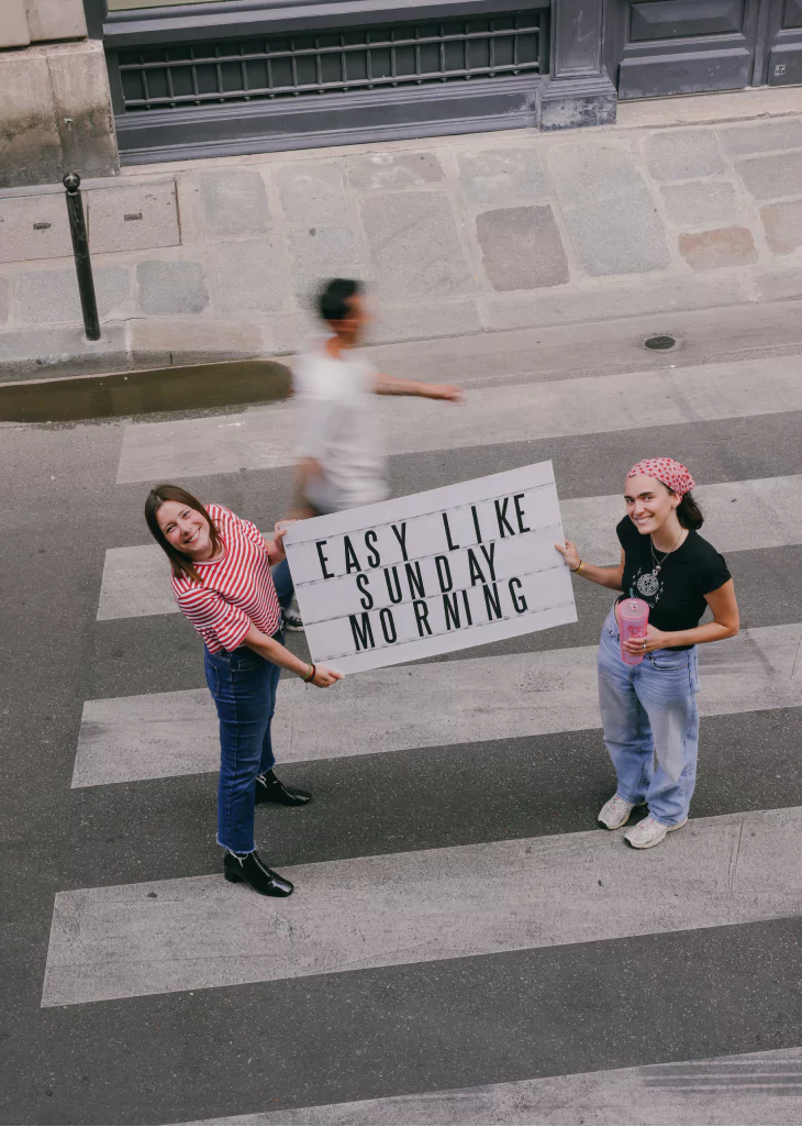 Photo de Camille et Charlotte qui tiennent un panneau "Easy like sunday morning" dans la rue